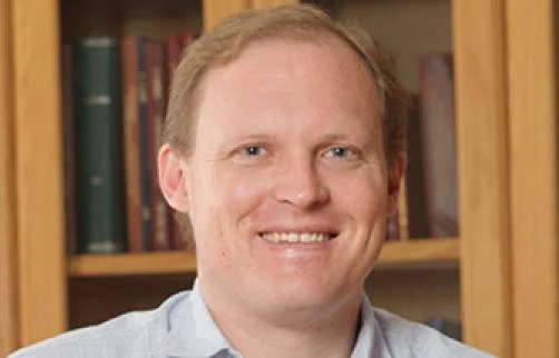 Stephen Coetzee in front of a wooden bookshelf.